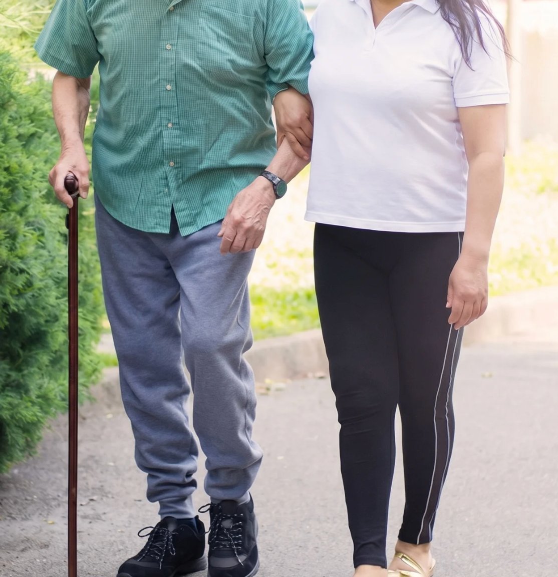 Pflegerin begleitet einen älteren Mann beim Spaziergang